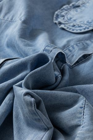 Сгънат плат на светлосиня дънкова риза, подчертаващ мекота и леко намачкана текстура